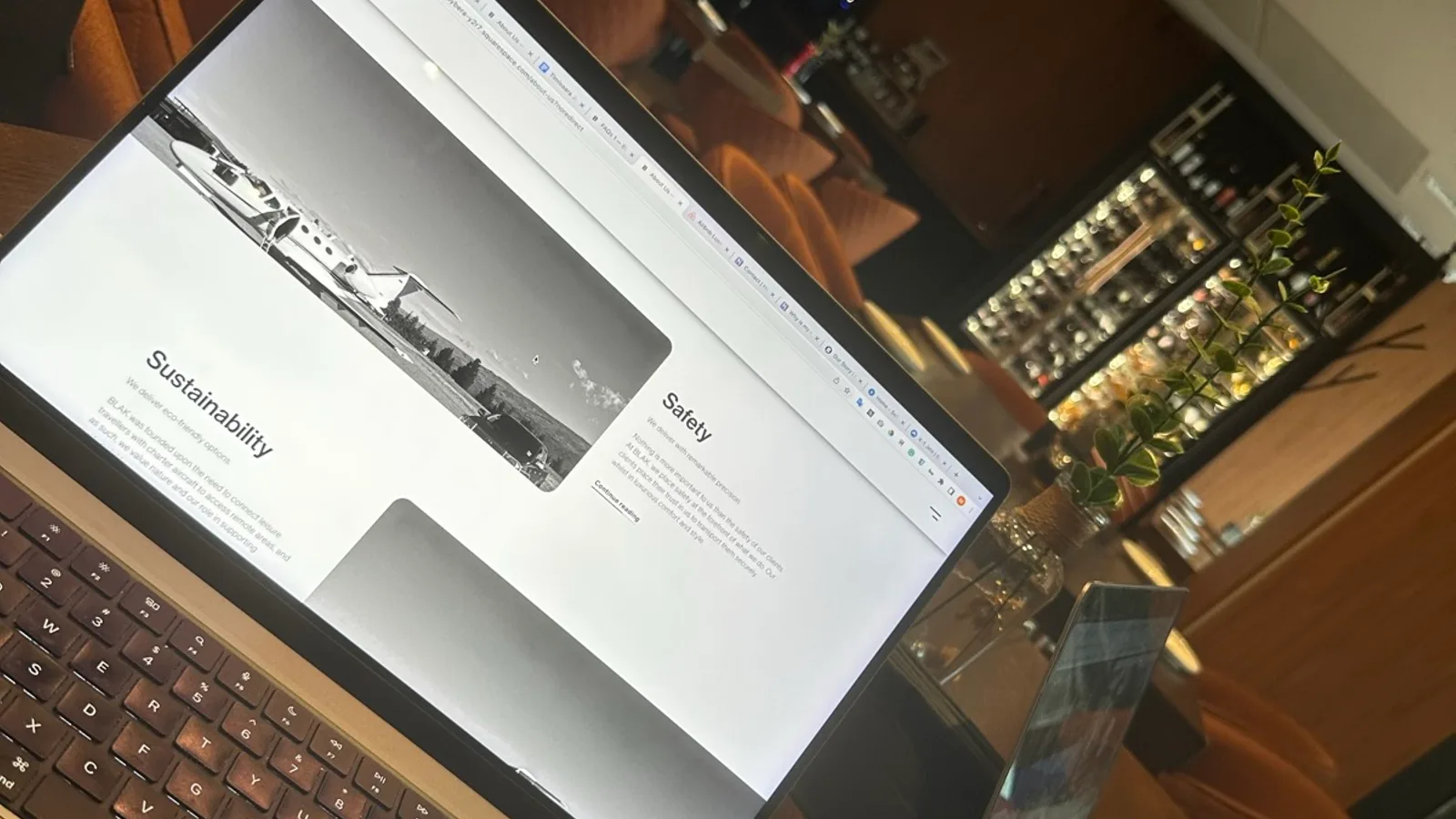 Two MacBooks on a hotel restaurant table during a working session, one showing the FLY JET BLAK website in progress